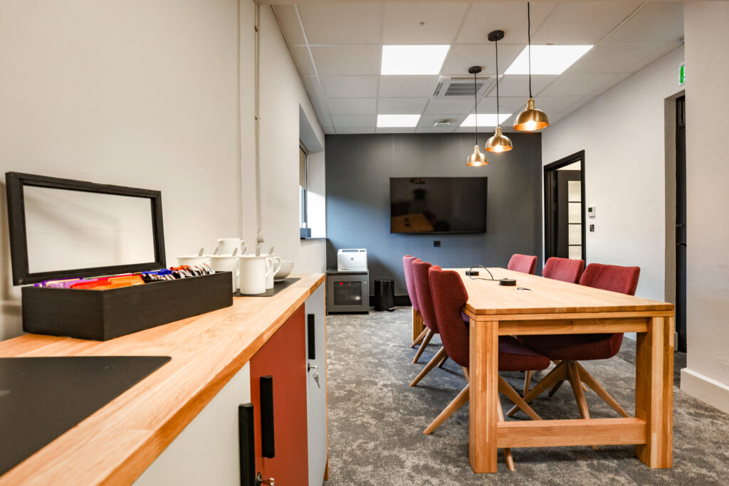 Small meeting area or coworking space. Large desk with six chairs, power access in the middle and an area for tea and coffee. TV on the wall to share presentations.