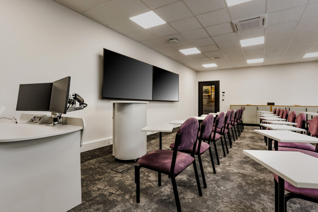 Space for presentations, collaboration, meetings or training. A photograph of a room with chairs and individual desks in front of a screen, complete with podium and computer control area.